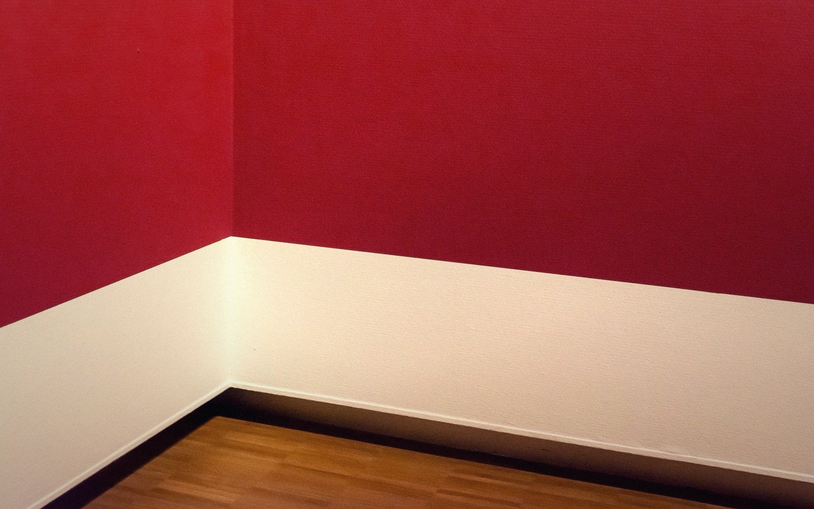 Corner of a room with dark red walls, white wainscoting and wood flooring