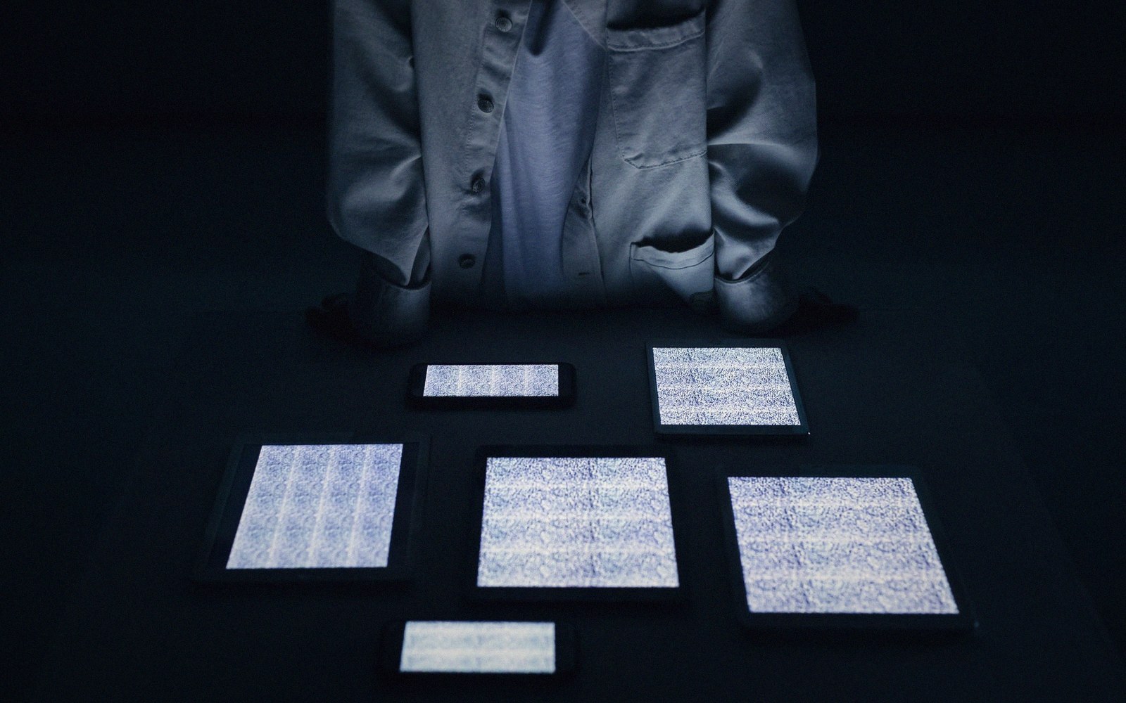 Person standing over several screens displaying static and noise patterns on a dark floor