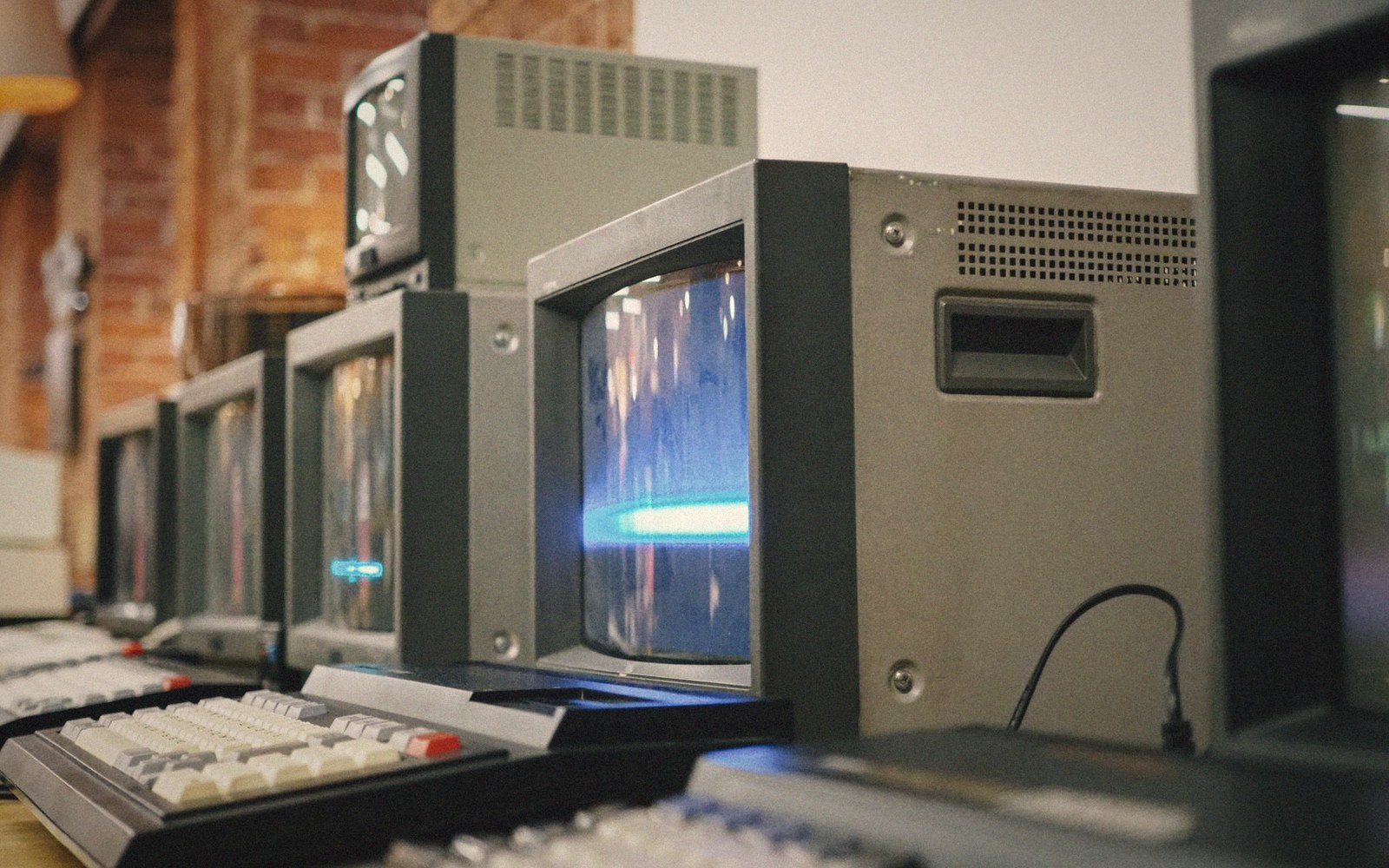 A row of vintage CRT computer terminals with keyboards displaying glowing blue screens