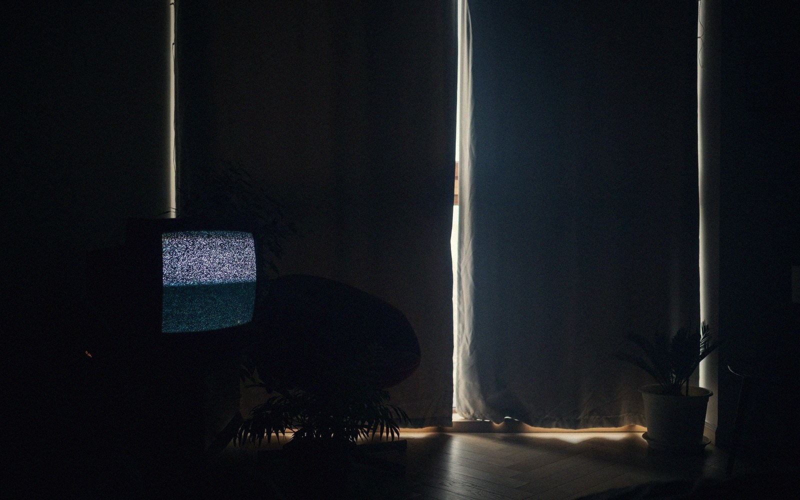 An old television displaying static glows in a dark curtained room