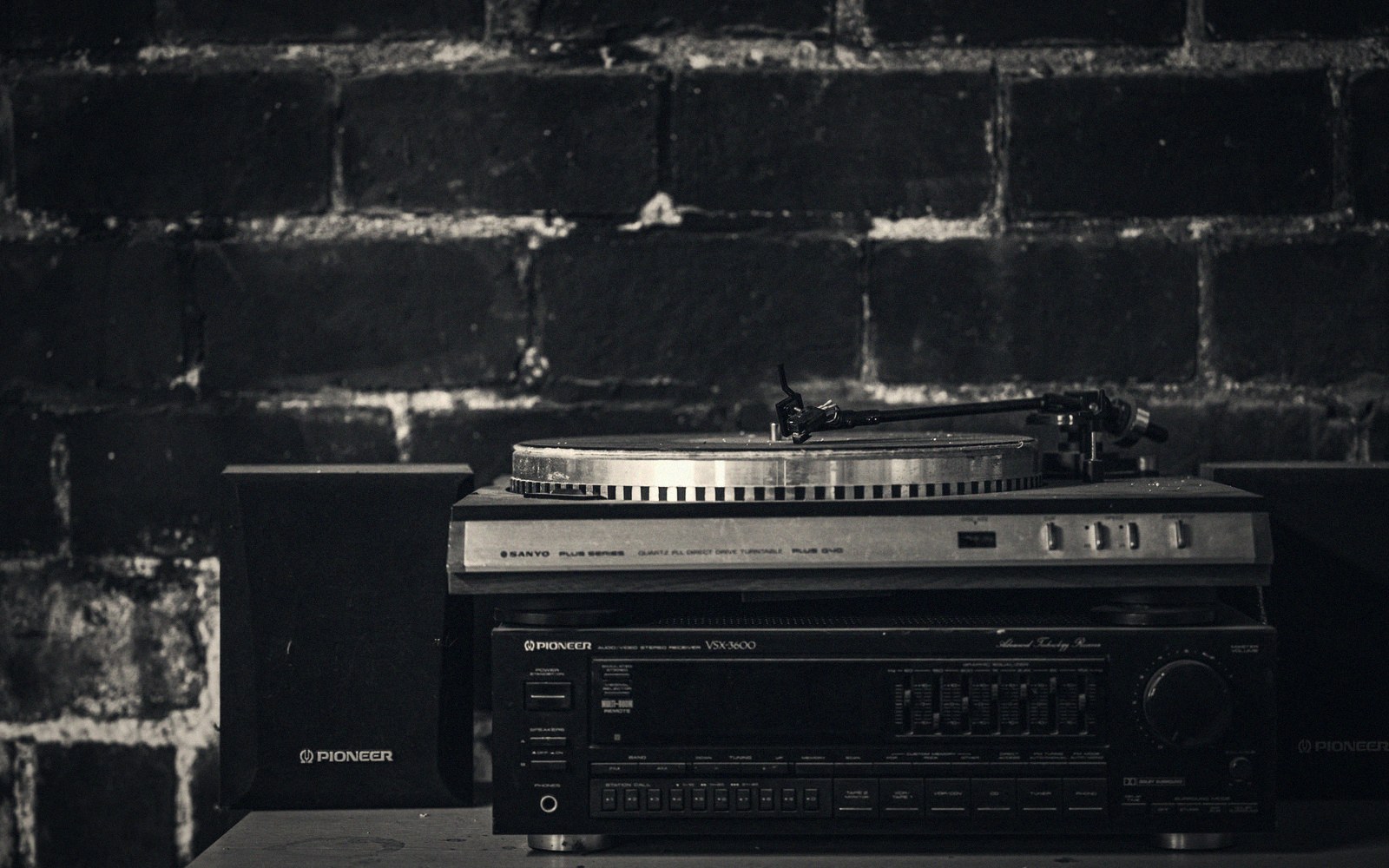 Turntable and Pioneer receiver stacked on speakers against a brick wall