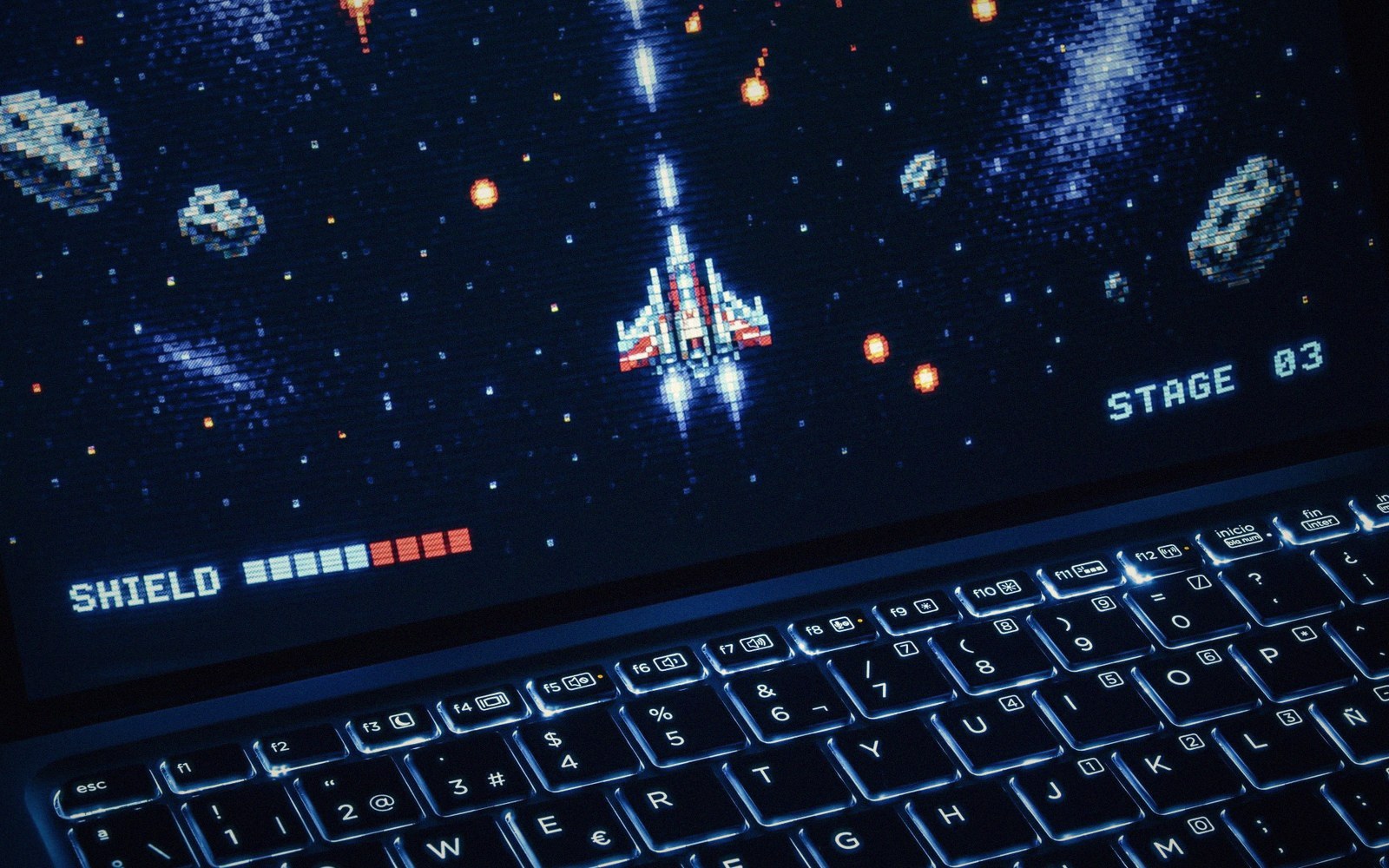 Retro space shooter game with a spaceship and asteroids displayed on a laptop screen