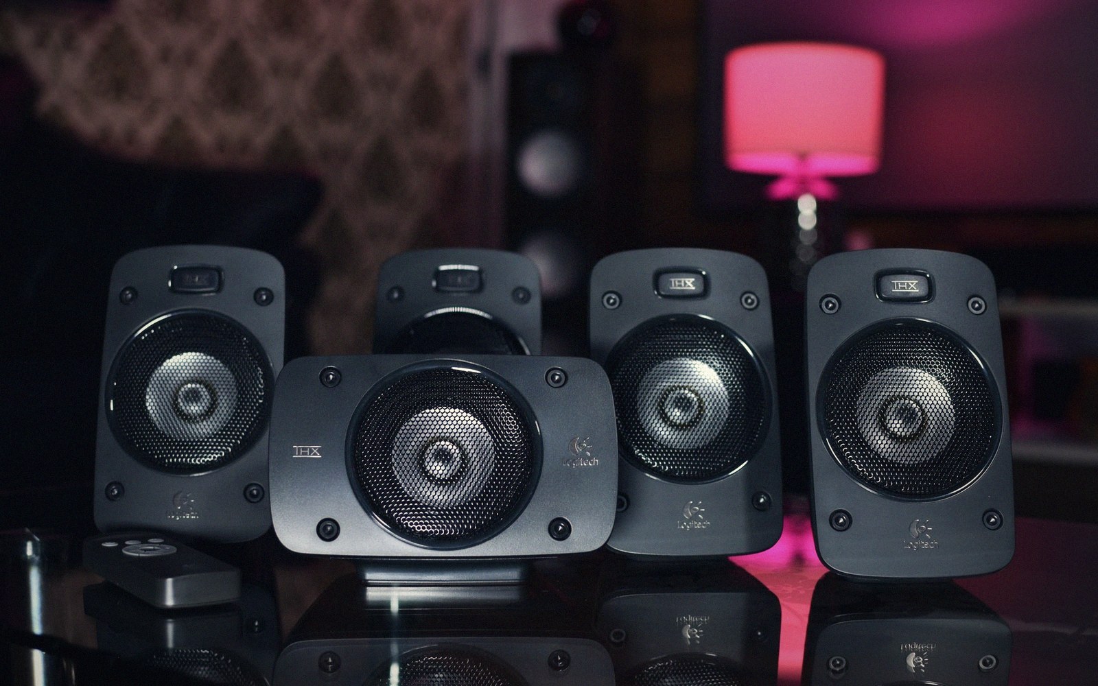 Five black Logitech THX satellite speakers arranged on a glass surface with a pink lamp behind