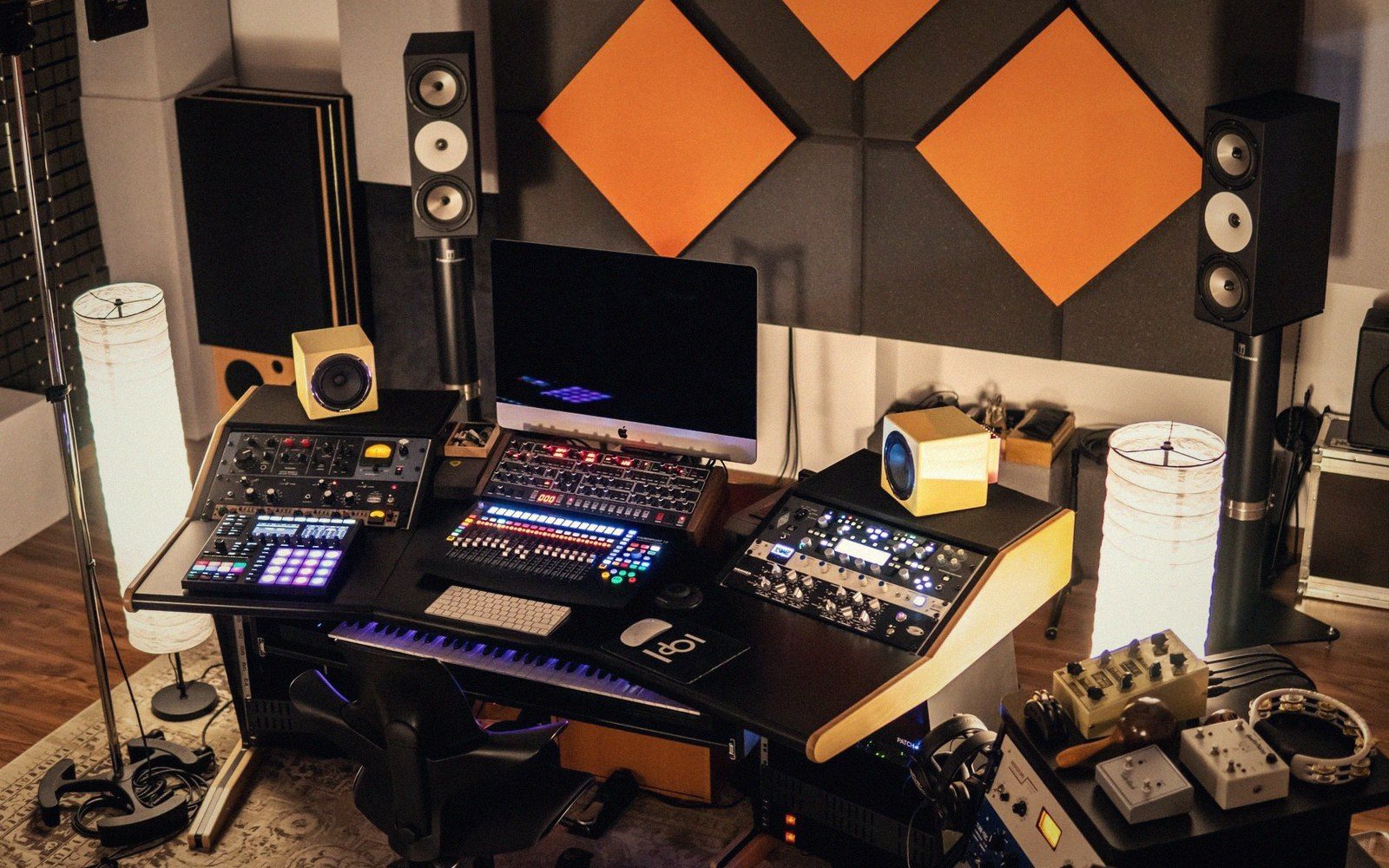 Home recording studio desk with mixing gear, monitors, and acoustic foam panels on the wall